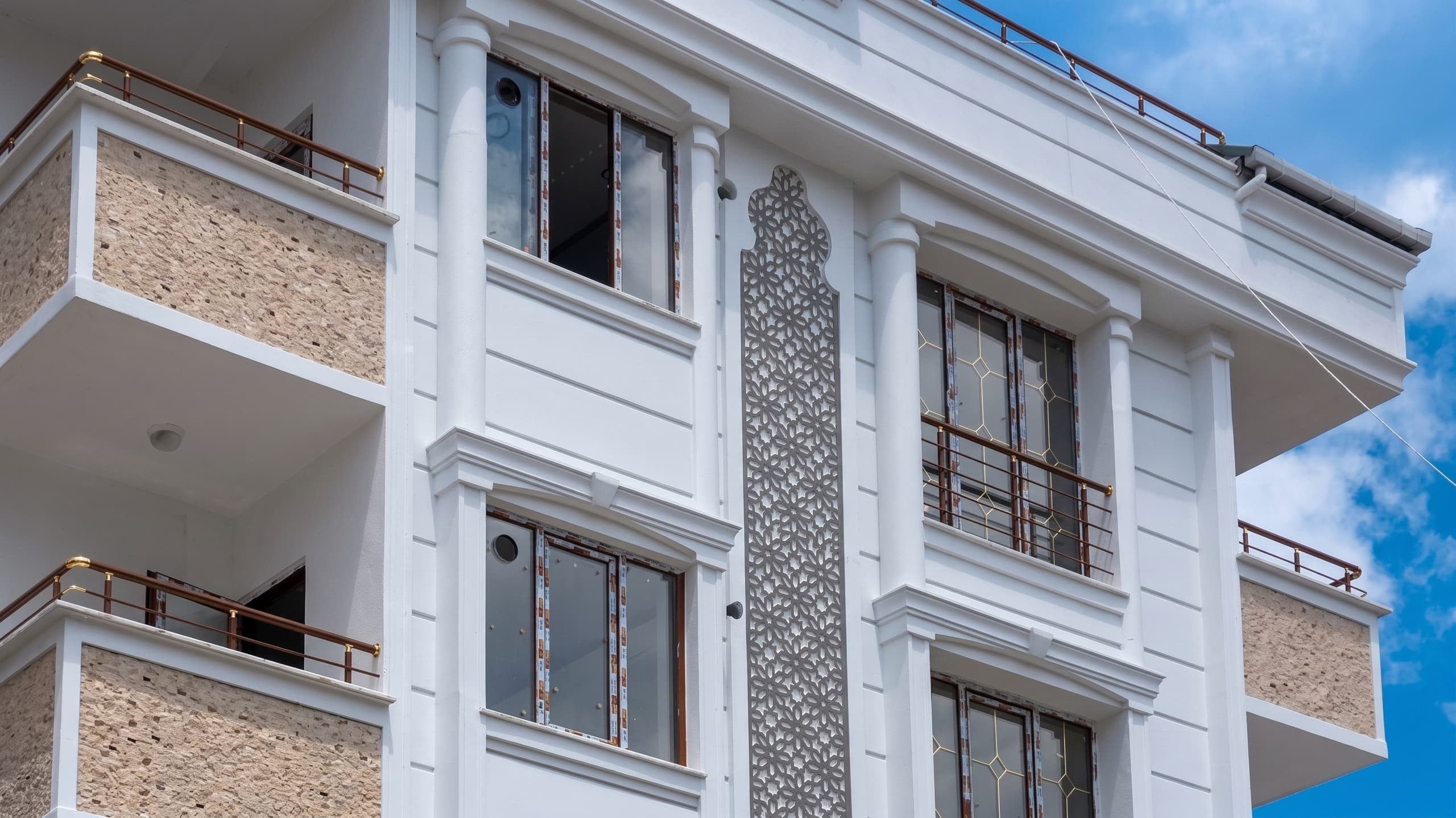 Ferforje korkuluklu balkonları ve işlemeli dikey cephe paneli olan konut bloğu